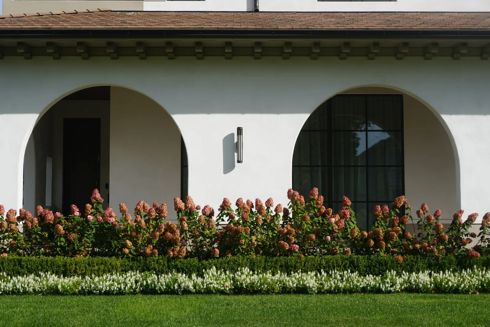 Hydrangeas above a clipped boxwood hedge and a band of white flowers along the arched loggia